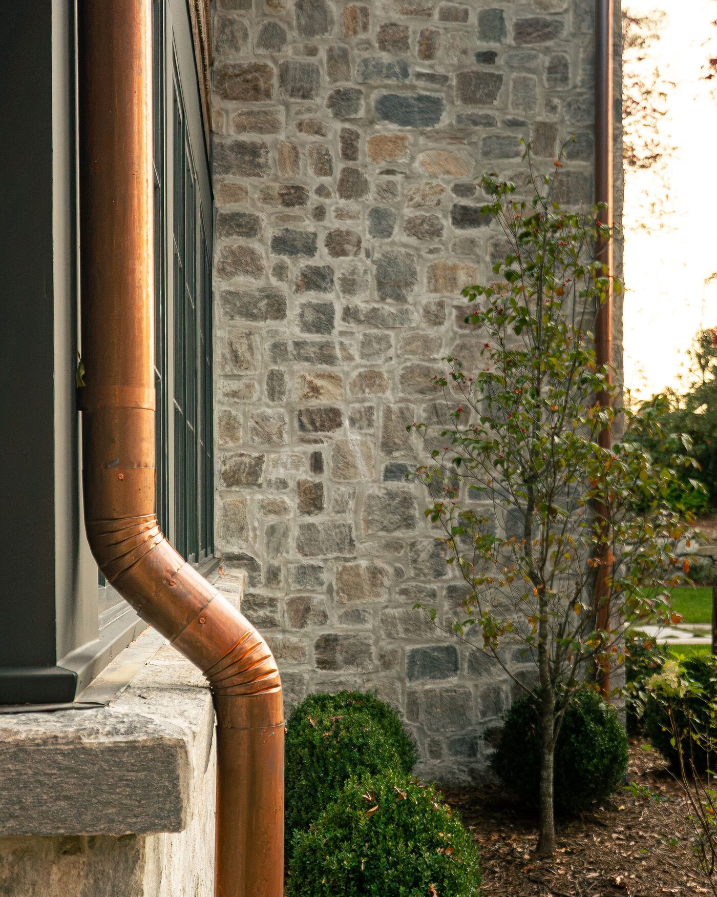 Copper downspout meeting hand-laid stone, Logan Custom Homes craftsmanship detail